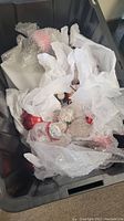 Large black storage bin filled with approximately 25 Christmas ornaments wrapped in bubble wrap and white tissue paper. Ornaments appear to be in good condition, mostly red and silver colors visible.