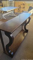 Side view of wooden entrance table showing curved side supports, flat top, and lower shelf with dark wood finish.