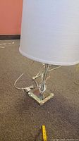 Full view of the glass lamp showing base and the white fabric lampshade on carpet flooring.