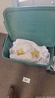 Open green plastic bin containing gold colored star-shaped ornaments laid on white tissue paper.