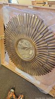 Full front view of the gold starburst metal mirror laid flat on the ground with some bubble wrap under the edges.