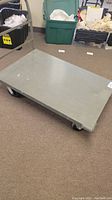Grey rolling cart rectangular platform with caster wheels on carpeted floor.