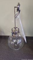 Front view of brand new hanging light fixture with clear glass globe on gray carpet background, showing chrome rod and mount.