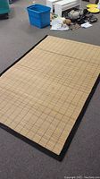 Full view of rectangular bamboo carpet laid flat on floor, showing woven bamboo slats and black border.