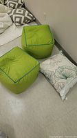 Overview photo showing two green ottomans and one pillow with leaf pattern.