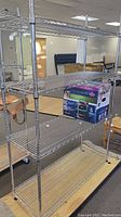 Metal wire rack with five shelves, shown in an indoor setting with packaging and furniture around.