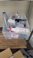 Plastic bin with assorted cleaning bottles and metal cable on a metal shelf