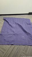 Photo showing a single purple moving blanket laid flat on carpeted floor, displaying quilted chevron pattern.