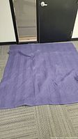 One dark blue chevron quilted moving blanket spread out on carpeted floor near a door, showing texture and size.