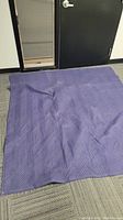 Purple quilted moving blanket spread on a floor in front of a door.