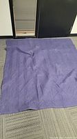 Single dark blue moving blanket spread out on floor, showing quilted zigzag pattern and texture.