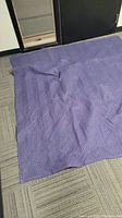 Photo of one dark navy or purple quilted moving blanket laid flat on carpeted floor, showing its texture and size.