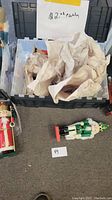Plastic storage container filled with approximately 12 nutcracker figurines, several wrapped in tissue paper. Two unwrapped nutcrackers are placed outside the box on the floor, one red and one green.