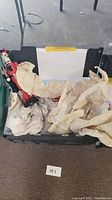 View of one large red and black wooden nutcracker figurine inside a black storage container with crumpled paper covering. Possibly other nutcrackers underneath paper.