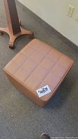 Brown square ottoman with stitched square pattern on top and smooth sides shown from two angles.