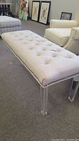Side view showing beige tufted upholstery and clear acrylic legs of bench