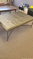 Full view of rectangular brown leather ottoman or coffee table with metal legs on carpeted floor.