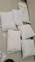 Six white decorative pillows laid out on floor showing plain and quilted fabric designs