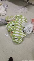 Green and white striped pillow with other textiles on floor.