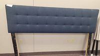 Photo of dark blue queen size upholstered headboard with tufted squares and wooden support legs.