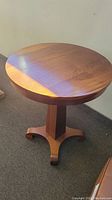 Round wooden table showing top and base details with natural light casting shadows.