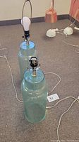 Two sea glass style glass lamp bases standing upright, showing cylindrical frosted glass design with metal lamp fittings at the top
