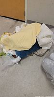 Pile of bedding items including yellow pillow sham, white pillow sham and cream bedspread on floor.