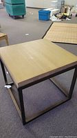 Square wood and metal table on carpeted floor surrounded by other furniture items.