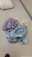 Set of three throw blankets (purple, beige, blue) piled with full size bedspread visible