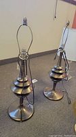 Two bronze colored lamps on carpeted floor, showing full height and design of lamps.