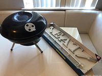 Small black charcoal grill with tripod legs and vented dome lid placed on table