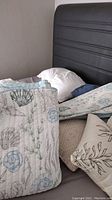 Photo showing the bed pillows, decorative pillows, and folded bedspread on the bed with a black headboard visible