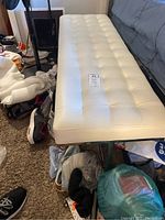 Side angle photo showing white tufted leather seat and metal legs, alongside shoes and other items on carpet floor.