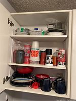 View of cabinet shelf showing stacks of plates, plastic bowls, disposable to-go cups (including Big Gulp), to-go foil containers with lids, and various small cups.
