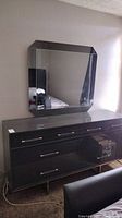 Full view of black speckled dresser with eight drawers and octagonal mirror mounted above.