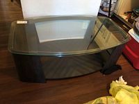 Full view of oval glass top coffee table showing glass surface and composite wood legs on hardwood floor.