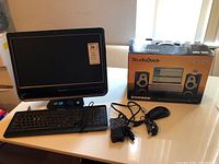 Lenovo all-in-one computer with keyboard, mouse, power adapter, and boxed Samson Studio Dock USB monitor speakers on a table.