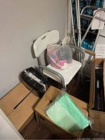 Photo of white shower chair, black folded item, green disposable pads on top of boxes