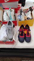 Four pairs of men's sports shoes placed on a mattress with their boxes, showing different color schemes and brands.