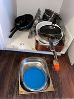 Photo showing nine pans stacked in a cabinet, with some lids and a muffin pan visible
