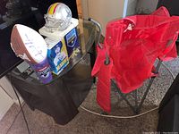 Wide view of sports collectibles on glass table with red folding tailgate chair behind.