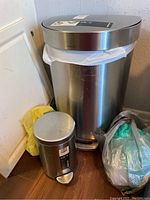 Photo showing two Simplehuman step-on waste baskets in stainless steel finish, one large and one mini size. The smaller mini bin is labeled 4.5L and both have foot pedals.