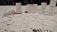 Photo showing unopened Clarins Paris skincare item boxes arranged on a lace tablecloth. Visible products include Extra-Firming Jour SPF 15 day cream and Re-Fresh eye and lip gel.