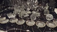 Various clear glass decorative items including finger bowls, candle holders, animal figurines, and cut glass pieces arranged on black fabric.