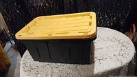 Image showing the large black storage tote with a yellow lid placed on a lace covered table.