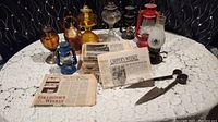 Vintage oil lanterns and sheep shears arranged on lace tablecloth with Collectors Weekly newspapers.