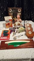 Full view of assorted vintage items including electric juicer box, handheld football game, doll, collectibles, wooden plaques, ceramic jars, and a model boat on a wooden base.