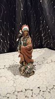 Full view of the 19-inch tall Native American statue on a lace tablecloth with a dark patterned backdrop.