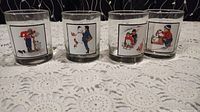 Four Norman Rockwell Pepsi collectable glasses displayed on crocheted tablecloth, each showing unique illustration.