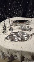 Overall view of the lot on a lace tablecloth showing three platters and two metal hooks